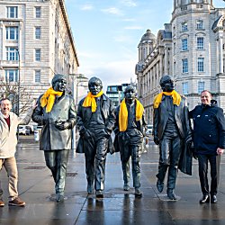 The Beatles Statue with yellow scarves around their necks and two people stood either side.
