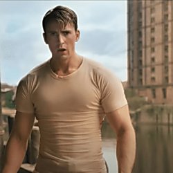 An image of a man acting as Captain America, wearing a white t-shirt with a brick building behind him.