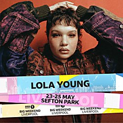 An image of Lola Young looking directly into the camera with their hands on their head with one palm under the other.