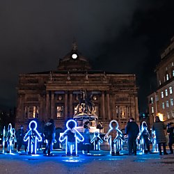 Light installations in the shape of people that are stood in a circle looking like they are holding hands.