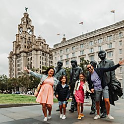 A family stand in front of the Beatles Statue on Liverpool Pier Head with the Liver Building in the background
