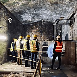 Inside the Mersey Tunnel Tour. People are wearing high vis vests and hard hats and look to be underground.