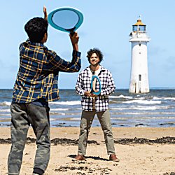 Two people playing tenning on a beach with a lighthouse in the background.