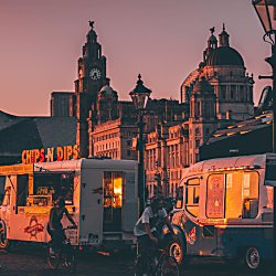 A sunset shot cross section with two retro food vans in the front with the view of the Royal Liver Building, Cunard and Port of Liverpool building in the background.