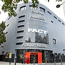 The entrance to FACT with threes lining the side of the building and a red arch leading people into the entrance of FACT.