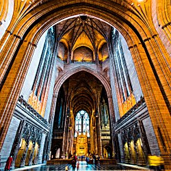 The interior of Liverpool Cathedral with a large stain glass window at the front and centre.