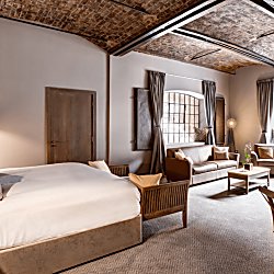 A hotel room with plush pillows and a large window with high ceilings.