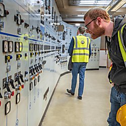 A person wearing a high vis yellow jacket looking at a control panel.