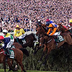 Jockeys and their horses making a jump over a fence at the Grand National Festival