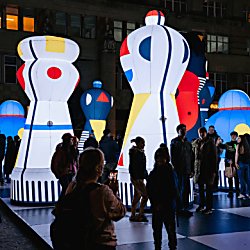 Colourful chess pieces all lit up with people walking around the base of the installation.