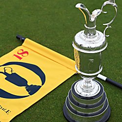 A silver trophy next to a yellow flag on the floor of some grass.