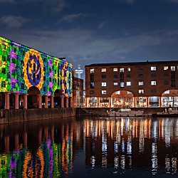 inside the Royal Albert Dock at night time with a colourful projection on the warehouse buildings