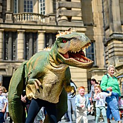 A person dressed up in a dinosaur costume with children and families around them.