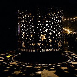 A round cylinder art work with cutouts of stars in it. Light shines out from the middle projecting stars onto the floor.