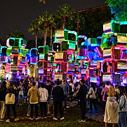 A light installation of stacked blocks in different colours with a crowd of people around it.