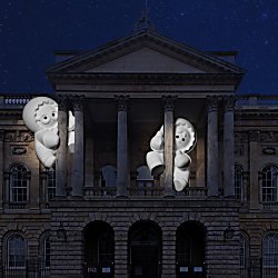 Two large characters glowing white clinging onto pillars at Liverpool Town Hall in the dark.