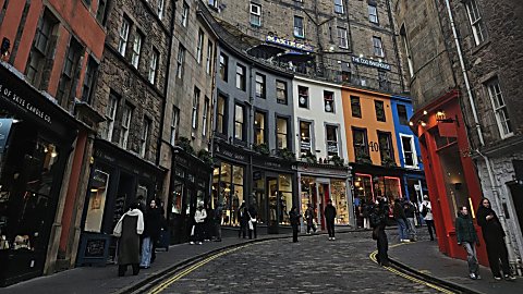 A street in Edinburgh with colourful shops outside, in yellow, blue and white.