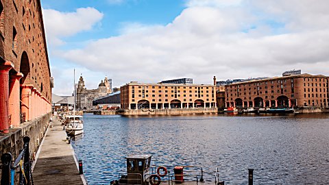 A large group of warehouse brick buildings with a dock of water in the middle of them. There are orange pillars to the left side of the buildings.