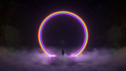 A large light installation that is a ring of rainbow light with a dark background and smoke across the floor.