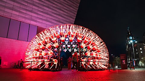 A large light installation that looks like a Dandelion lit up in red colours.