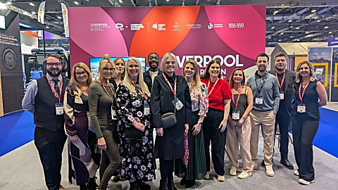 A group of people standing on a tradeshow stand with a bright pink stand behind them saying 'Liverpool'.