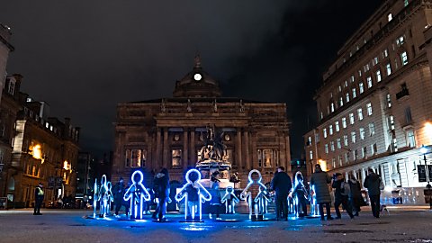 Light installations in the shape of people that are stood in a circle looking like they are holding hands.