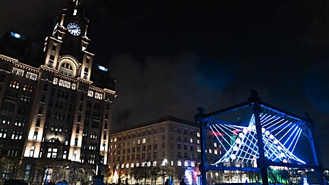 A large light installation that looks like a large pendulum outside of the Royal Liver Building.