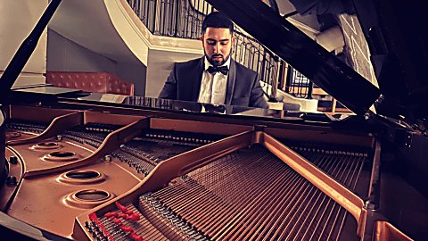 A man wearing a tuxedo sits at a grand piano which is open