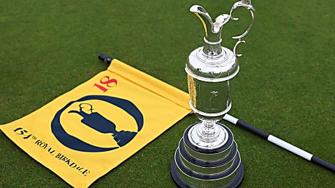 A silver trophy next to a yellow flag on the floor of some grass.