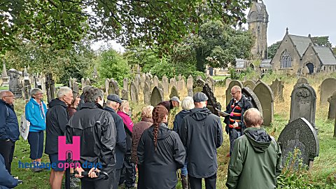 A crowd of people stand with a tour guide in a church graveyard