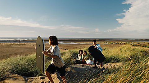 A family of four on a sand dune at a beach with surf boards.
