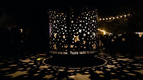 A round cylinder art work with cutouts of stars in it. Light shines out from the middle projecting stars onto the floor.