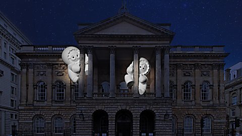 Two large characters glowing white clinging onto pillars at Liverpool Town Hall in the dark.