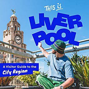 Promotional graphic showing a person sitting on a rooftop terrace and pointing toward the Royal Liver Building clock tower in Liverpool under a clear blue sky. Large bold blue text reads “THIS IS LIVERPOOL,” with smaller white text below saying “A Visitor Guide to the City Region.”