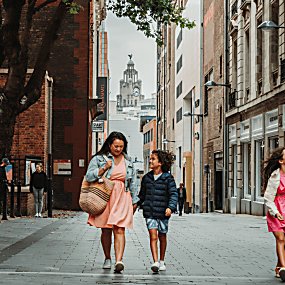 People are walking down a street in Liverpool city centre. They are laughing together and the Royal Liver Building is framed in the background of the shot