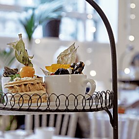 A stand with a selection of cakes on a plate. There is a person in the background and fairy lights.