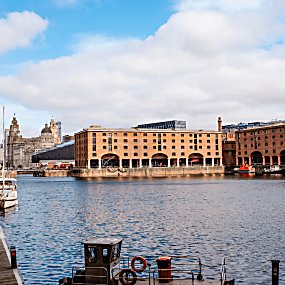 A large group of warehouse brick buildings with a dock of water in the middle of them. There are orange pillars to the left side of the buildings.