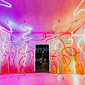 A large pink room with ribbon patterns in colours on the walls and in led lights from the ceiling