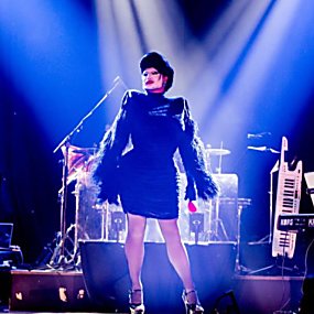 Danny Beard on stage in drag surrounded by a band with blue lights on them