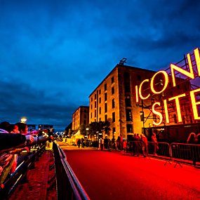 A large red neon sign that reads 'ICONIC SITE' alongside the Royal Albert Dock warehouses