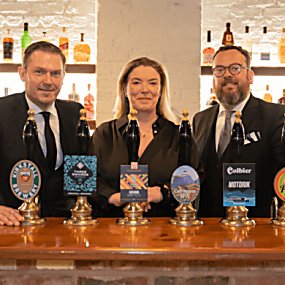 Three people standing smiling behind a bar.