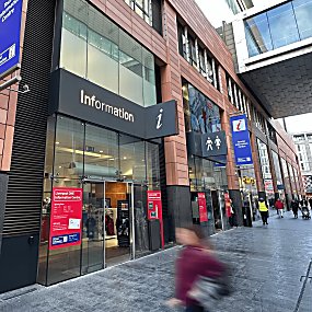 Liverpool Tourist Information Centre exterior image with people walking past the entrance. Outside there is a sign above the door which says 'Information' in silver writing.