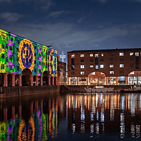 inside the Royal Albert Dock at night time with a colourful projection on the warehouse buildings