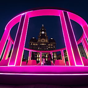People inside a pink recreation of the eurovision stage on Liverpool Waterfront with the Liver Building in the background