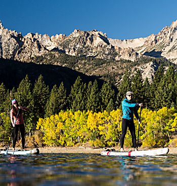 Couple stand-up paddleboarding on a lake with colorful gold aspens trees and mountain peaks behind them