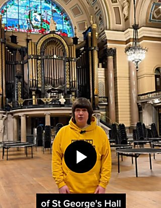 A person wearing a yellow jumper inside a large room inside St George's Hall with an organ on the back wall behind them.