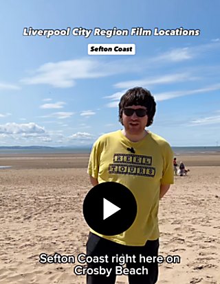 A person wearing a yellow t-shirt stood on a beach with blue sky behind them talking to the camera.