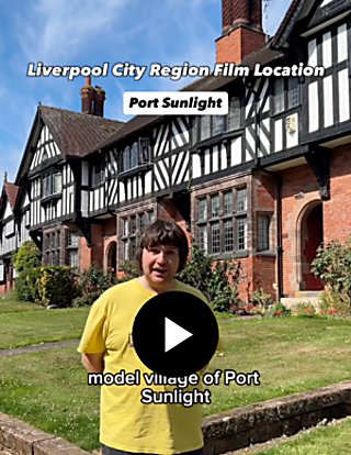 A person wearing a yellow t-shirt stood in front of a Tudor House with a grass garden in the front.