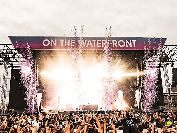 A stage with pyro and confetti shooting into a crowd of people with their arms in the air