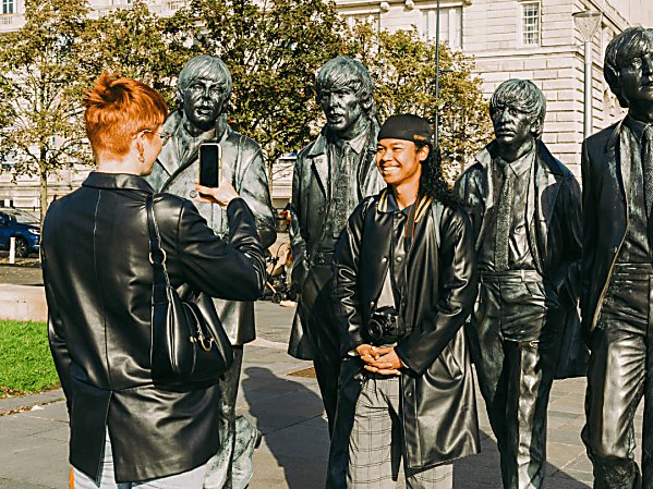 A girl takes a picture of her friend next to a large bronze statue of the Beatles